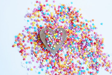 sweet colorful confectionery sprinkling and wooden heart on light background. heart - symbol love, romance, Valentine's day. minimal creative concept. template for design. top view