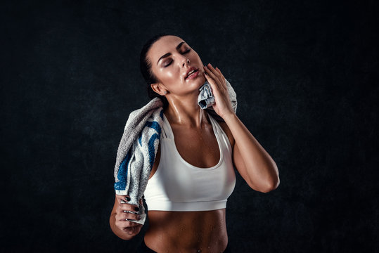 Attractive athletic young woman with perfect body wearing sportswear is posing with a towel against black background. Beautiful fitness girl relaxing after workout.
