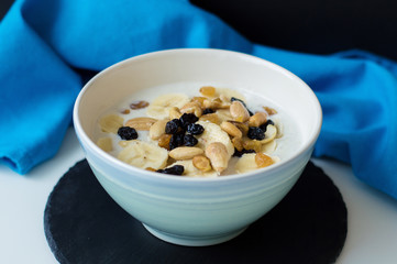 Oatmeal milky porridge with variety of nuts and raisin in a blue bowl. Blue napkin and slate board