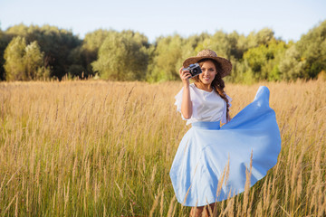 Girl in hat shooting photo walking in golden dried grass field with camera