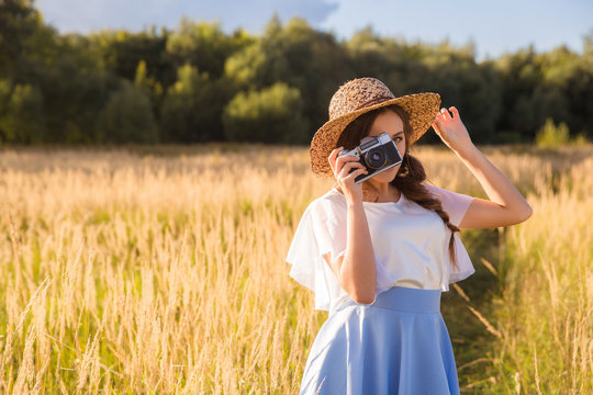 Girl in hat shooting photo walking in golden dried grass field with camera