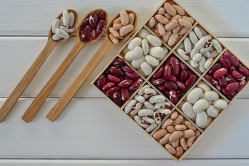 Assortment of beans in wooden box on white wooden background 