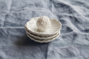 Close-up of white coconut candy in the shape of a ball on a white saucer in the form of shells on blue background.