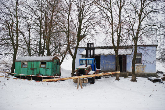Rusty old soviet tractor covered by snow against working booth.