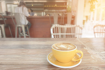 A cup of coffee latte on wooden table in warm cafeteria