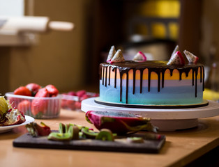 chocolate cake with multicolored shortcakes decorated by dragon fruit with Organic fresh kiwi fruit and half of dragon fruit  on a wooden cutting board,red ripe strawberry in plastic box