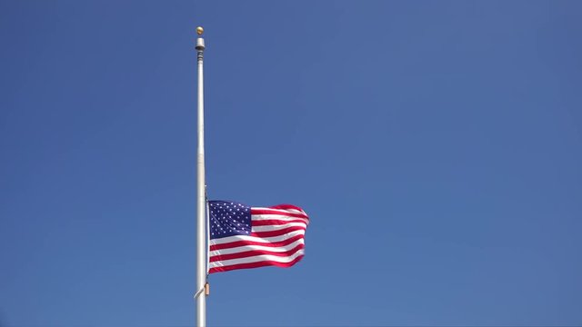 American flag flying at half mast aka half staff against a clear blue sky