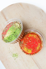 Two jars of colorful spices on a wooden background.