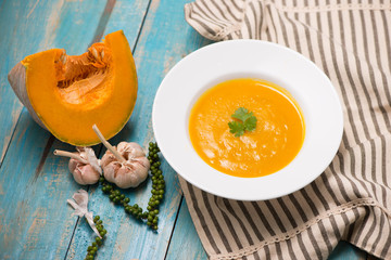  Top view of pumpkin and carrot soup with cream and parsley on blue  wooden background.