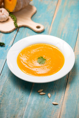  Top view of pumpkin and carrot soup with cream and parsley on blue  wooden background.
