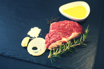 Raw beef steak on a cutting board with rosemary and spices.