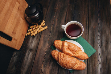 drink in a cup, croissants in a plate, teapot and sweet rolls on a table