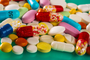 Multicolored pills and tablets on green background
