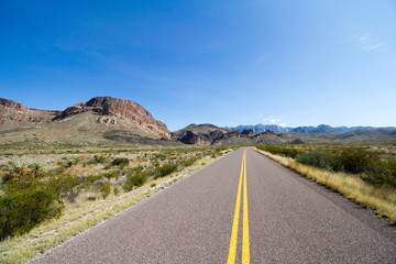 A road disappears in to the distant mountain scenery and invites someone to go on an adventure or road trip, and suggests general wanderlust