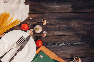 knife and fork on a plate, spaghetti and red tomatoes on a table
