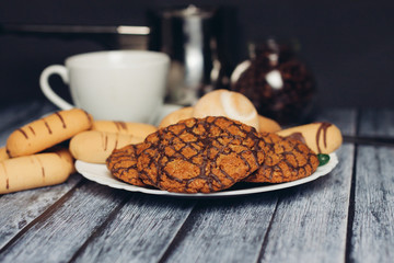 Sand and oatmeal cookies in a plate, mug on a wooden background