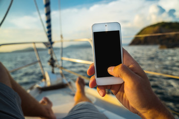 Rest on a yacht with a phone in hand. Summer leisure. Male lying on the deck and enjoy your smartphone. The guy doing the photo feet on the background seascape and yachts. - Powered by Adobe