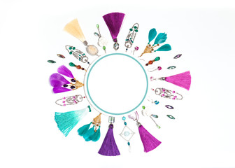 Handmade turquoise and violet bijouterie circle garland with earrings,necklace, gems, tassels and feathers in boho style, lying flat on the white background, top view, with round empty place for text