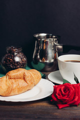 iron ladle in the background, croissants, a cup with a drink and a flower