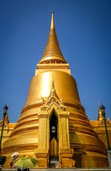 Fototapeta premium Tourists with umbrellas in front of the Golden Stupa in the Grand Palace in Bangkok