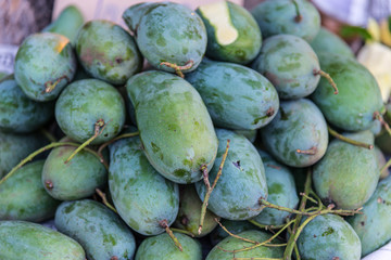 Bunch of green and ripe orange mango on table. Selective focus on orange mango. Selective focus