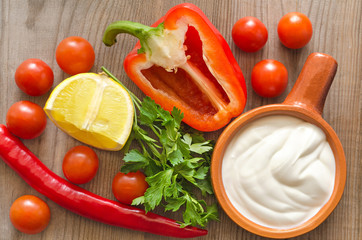 Ceramic dishes with sour cream, and ingredients for salad on an old wooden table.