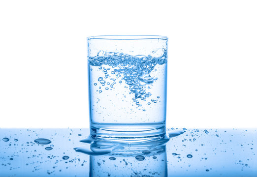 water in transparent glass with drops and bubbles isolated over white, blue background, close up