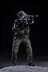 Soldier aiming from rifle on dark background/Soldier in uniform, body armor and helmet holding rifle  on dark background