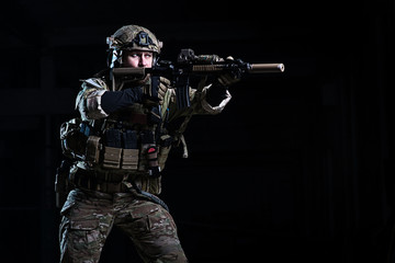 Soldier with rifle aiming at target/Man in body armor, helmet with rifle on dark background