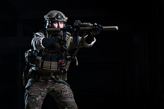 Soldier with rifle aiming at target/Man in body armor, helmet with rifle on dark background