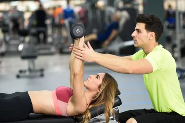 Gordijnen Personal trainer helping a young woman lift weights © javiindy