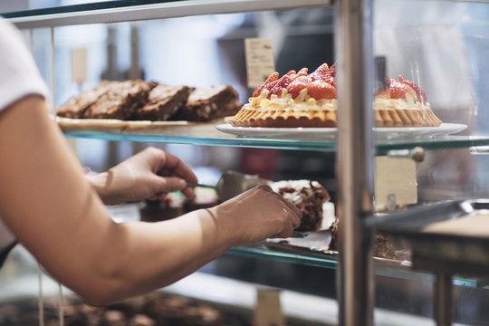 Woman baker arranging cakes at coffee shop showcase.