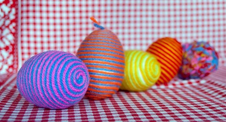Easter multicolored decorative eggs with wrapped yarn on checkered textile background, close up. Easter decoration.