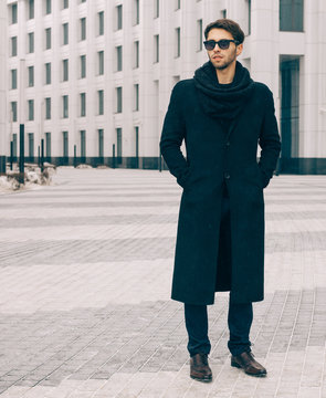 Fashion and Style. A young man in a fashionable black coat and sunglasses posing near the business center