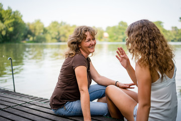 Cheerful mother and daughter sitting on the edge of a wooden jetty