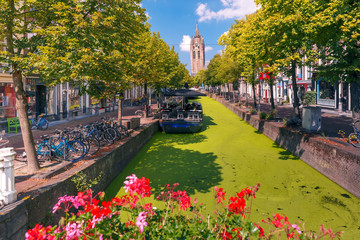 The picturesque Oude Delft canal and leaning tower of Gothic Protestant Oude Kerk church on a sunny day in Delft, South Holland, Netherlands.