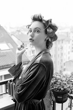 Bellissima ragazza in vestaglia fuma una sigaretta sul terrazzo  