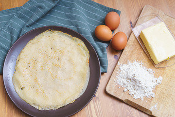 Ready traditional thin pancakes on a plate with ingredients and decor.