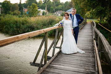Cheerful wedding couple on wooden bridge at sunset.