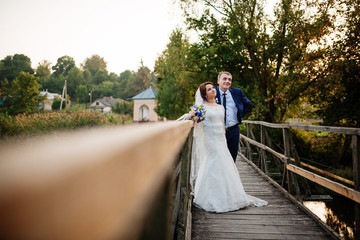 Cheerful wedding couple on wooden bridge at sunset.