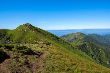 Hiking trail leads along the rocky ridge among the green alpine meadow