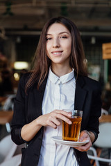 young cute brunette girl business in the interior hipster cafes holding a glass of tea.