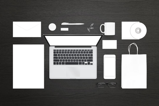 Visual identity design presentation template. Top view of laptop computer, mobile phone, stationery and office supplies. Top view of black wooden desk.
