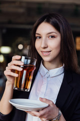 young cute brunette girl business in the interior hipster cafes holding a glass of tea.