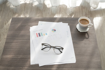 office table with modern glasses on business report chart paper and cup of coffee, concept of business lifestyle.