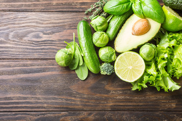 Background with assorted green vegetables, salad, avocado, cucumber, lime and Brussels sprouts on wooden table top. Healthy food concept with copy space.