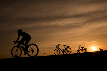 Obraz premium Silhouette of a cyclist and vintage bikes against sunset background in Thailand.