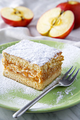 Apple pie piece on a plate with fresh apples in background