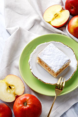 Apple pie piece on a plate with fresh apples in background