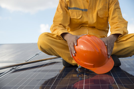 Closeup Of Engineers  Or Worker Hold In Hand Orange Helmet Wearing Orange Bear Coat. Sitting On A Solar Cell.